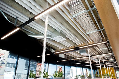White baffles fixed below a concrete soffit, running between cable trays, ductwork and linear light fittings.