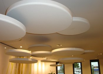 Circular white ceiling rafts suspended at two different heights in a room with glazing along one wall.