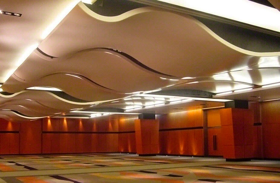 Curved white rafts below the ceiling of a banqueting room, with timber panelling along the walls.