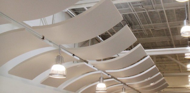 Curved white baffles suspended below a metal deck soffit, with pendant light fittings hung between them.