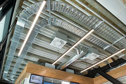 White baffles below a concrete soffit in a double-height space, threaded between cable trays and round ductwork.
