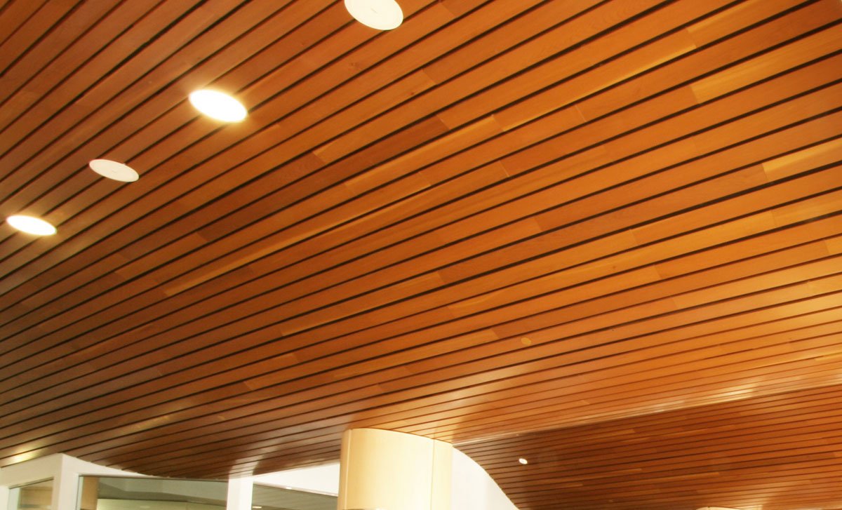 Close view of a timber slatted ceiling with open joints between the slats and recessed downlights.
