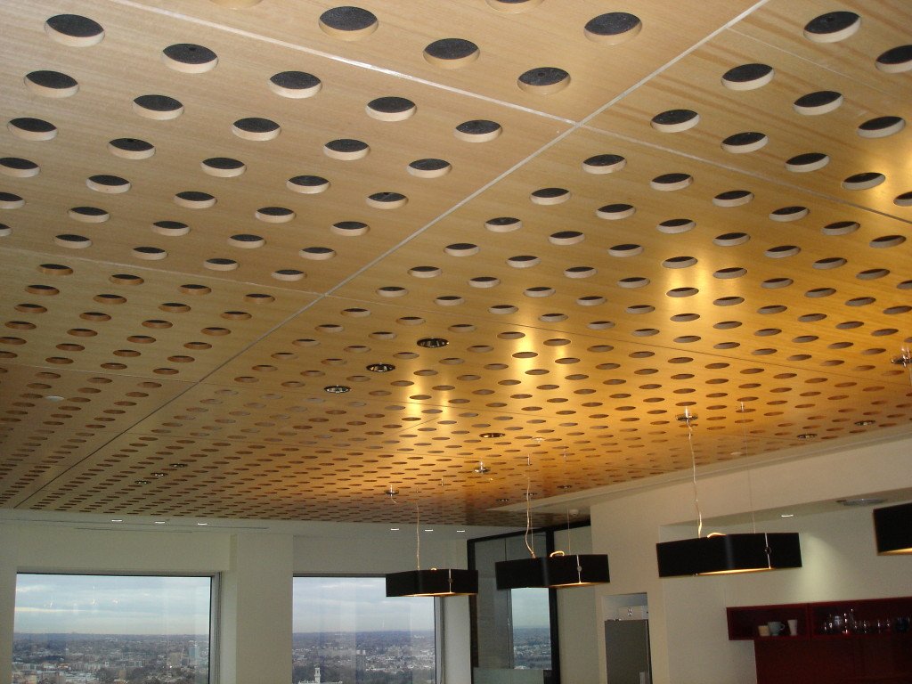 Timber ceiling panels drilled with circular perforations, lit by recessed downlights, above an office with glazing to the city beyond.
