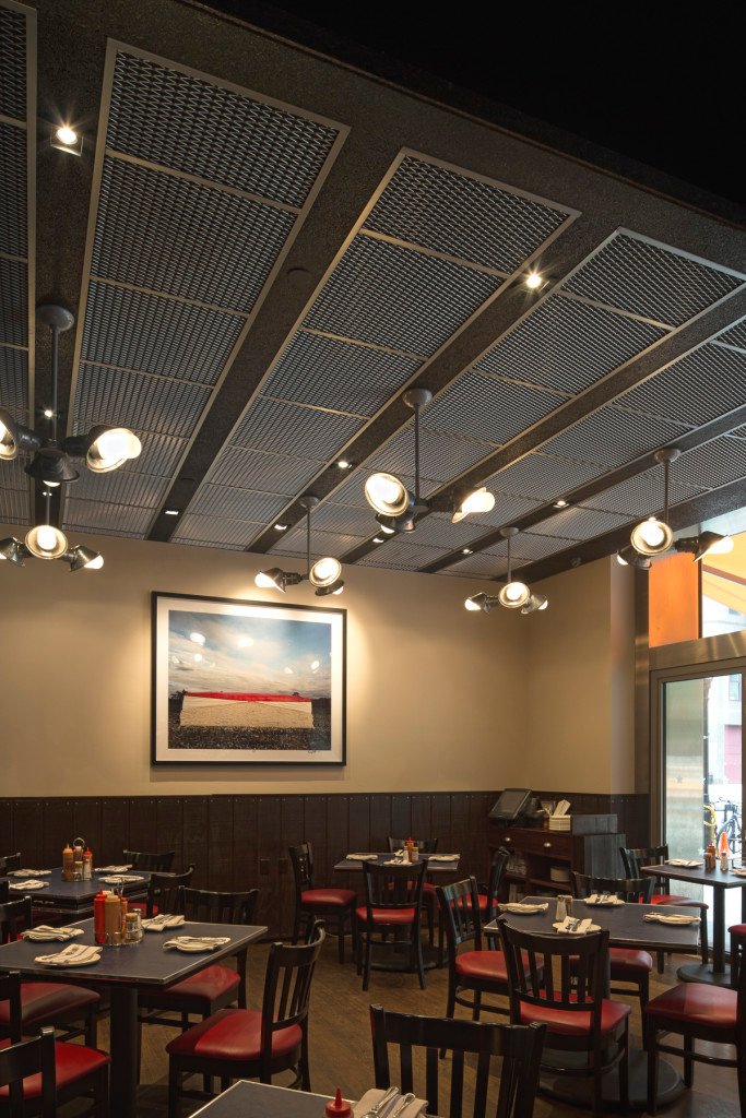 Metal mesh ceiling panels framed in a grid above a restaurant dining room hung with pendant lights.