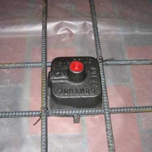 A black isolator mount sitting within a grid of steel reinforcement bars laid over a slab.