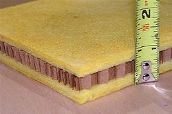 A cut section of layered isolation board with a tape measure showing its thickness.