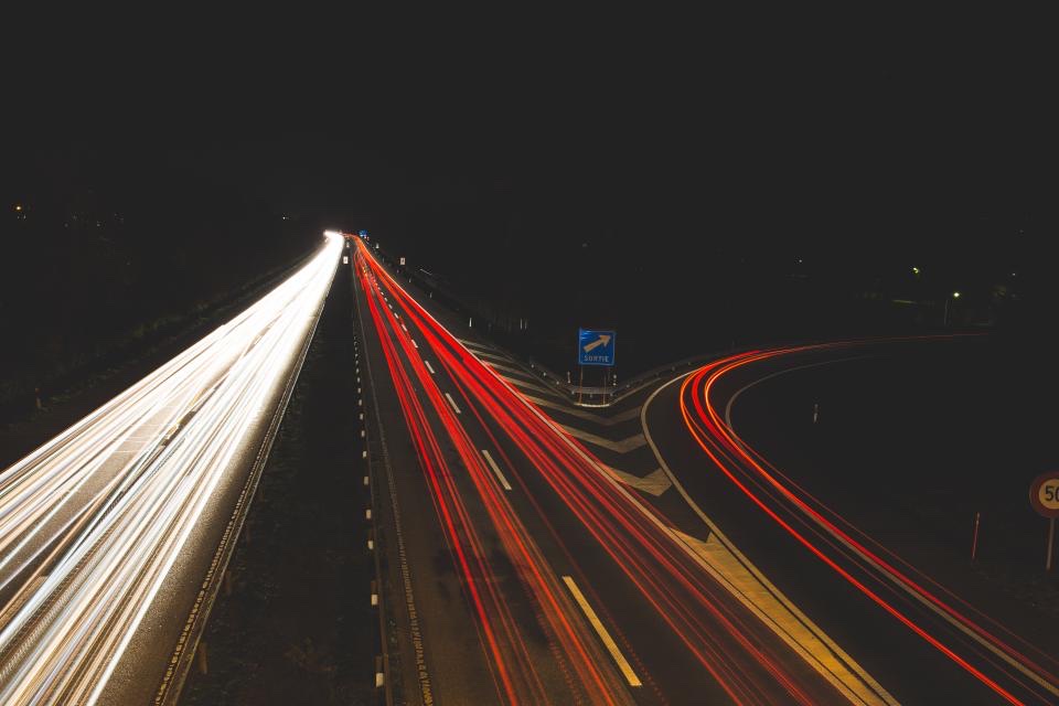 A long exposure of a dual carriageway at night, headlight and tail-light trails running across the frame.