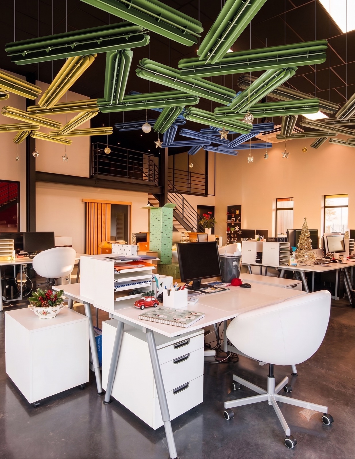 An open-plan office with clusters of green, yellow and blue acoustic baffles suspended over the desks.