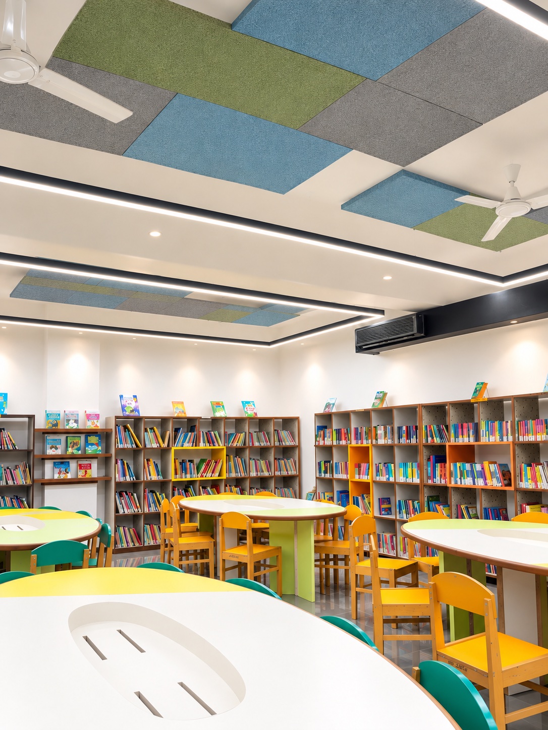 A school library with coloured acoustic panels set into the ceiling, book stacks and reading tables below.