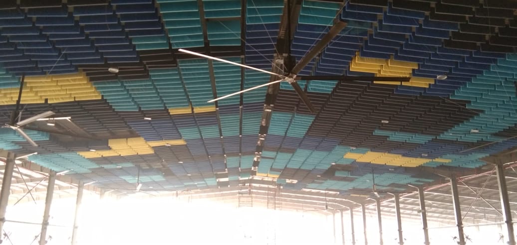Ceiling of a large hall filled with blue, green and yellow acoustic baffles hung between steel trusses